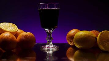 Rum drink being poured into long glass, isolated on colorful lighted wall background. Stock clip. Alcohol drink on the reflective table or bar counter with orange fruits. video