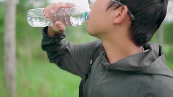 el caminantes fueron cansado y detenido a bebida Fresco agua. Seguir a descanso y bebida agua en naturaleza. joven asiático mochilero de viaje en el bosque, sediento para felicidad, divertido y sonrisas video