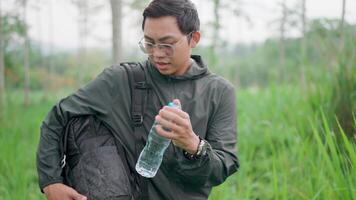 das männlich Reisender wurden müde und gestoppt Trinken sauber Wasser. jung asiatisch Backpacker Reisen im das Wald sich ausruhen und trinken Wasser, dann fortsetzen Wandern inmitten Natur video