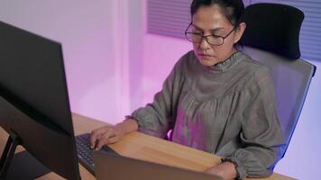 Freelance web designer sitting at desk in evening working, wondering about abnormal behavior of code on laptop computer, writing javascript binary code on workstation at work video