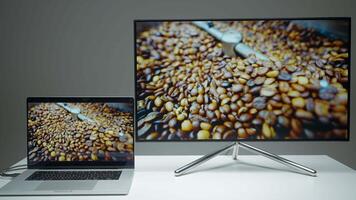 Laptop transmitting an image via hdmi on a TV screen. Action. Computer and new tv on a table isolated on a grey wall background. video