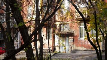 Bare trees in the courtyard of a residential building. Stock footage.A bright red apartment building with an entrance and leaves that hang from the bushes. video