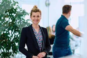 Portrait of a Blonde Businesswoman in a Modern Office with Her Workspace and Colleagues in the Background. photo