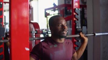 African american bodybuilder doing squats using a barbell in a gym to train his legs and back. Powerful fitness workout video
