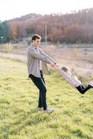 Smiling dad twists little girl by the hands on a sunny autumn meadow photo