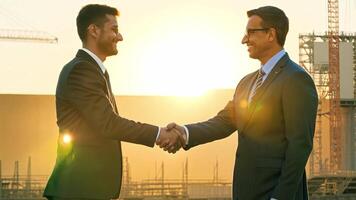 Two Businessmen shake hands on a deal with view of The background of a large construction site has beautiful sunlight. video
