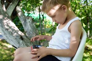 blonde-haired child engrossed in the use of a handheld device, his hunched posture potentially straining his developing spine as he remains sedentary photo