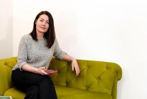 Smart and professional girl enjoying a productive working day, relaxing on a stylish sofa in a modern office with a tedephone in her hands photo