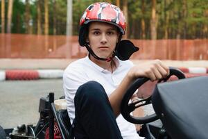 young man sits behind the wheel of a go-kart, his expression focused and determined as he prepares to race around the track, embracing the thrill of high-speed, adrenaline-fueled driving photo