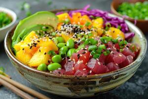 A colorful poke bowl featuring fresh tuna, diced mango, edamame, roe, purple cabbage, and avocado in a ceramic bowl, topped with sesame seeds and green onions. photo