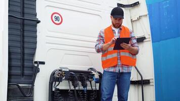 Professional truck driver checking using tablet computer and standing by long vehicle. Transportation service video