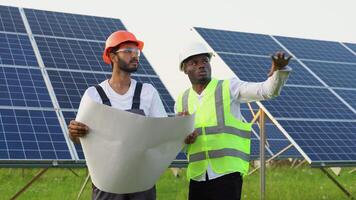 Young african engineer and indian technicians standing and planning to installing solar panels. Industrial workers discussing on solar system installation video