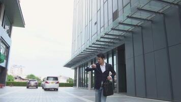 asiático empresario mira a su reloj en un prisa como él carreras a captura arriba con el reloj detrás un alto edificio. video