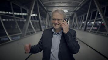 Sophisticated businessman in a suit talking on cellphone while walking in covered walkway video