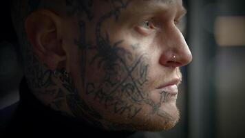 un tatuado hombre con cara tatuajes es desplegado en un urbano configuración, acompañado por artístico elementos video