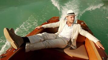 A man is relaxing on a boat in stylish attire, wearing a white hat on a sunny day video
