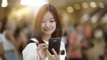 A young woman is using her smartphone in a crowded public space with a blurred background video