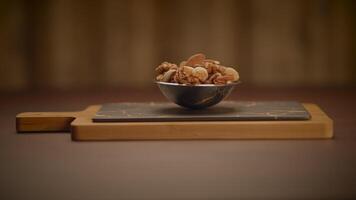 A wooden cutting board with assorted nuts in a steel bowl set on a dark background video