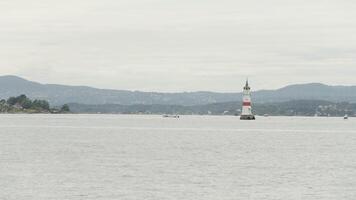 Picturesque natural landscape with a lighthouse and rippling water surface. Action. Cloudy sky above ocean and mountains on the background. video