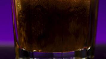 Pouring Cola with bubbles into the glass, close up. Stock clip. Coke soda in transparent glass on a colorful lighted wall background. video
