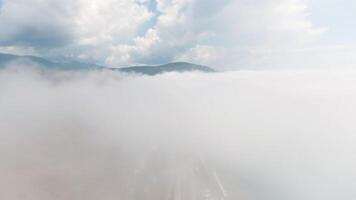 Top view of thick clouds with mountain peak on horizon. Schot. Flying in cloudy sky with dense clouds from top of mountain. Landscape of top of green mountain on horizon among white clouds video