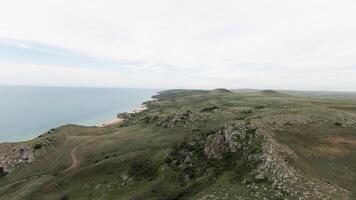 Top view of hilly coast on background of sea horizon. Shot. Coast line with hills and sparse grass with sea. Sea horizon line with coast. North coast in summer video