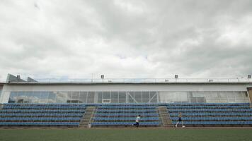 Sports field with training athletes with empty seats and cloudy sky on the background. Stock footage. Concept of olympic games, sport, and active lifestyle. video