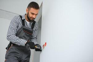 Electrician Builder at work, installation of sockets and switches. Professional in overalls with an electrician's tool. Against the background of the repair site photo