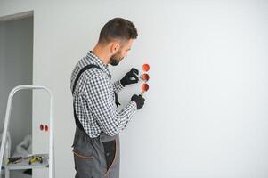 Serious male electrician installing power socket in the apartment and using screwdriver photo