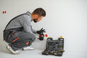 Serious male electrician installing power socket in the apartment and using screwdriver photo