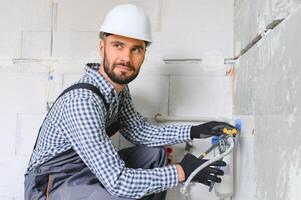 Horizontal snapshot of young plumber working with grey sewer pipes, fixing them to wall with a help of screwdriver. photo
