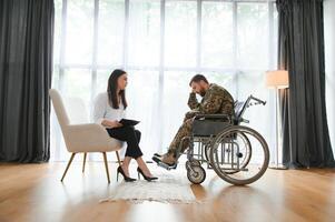Depressed guy in camouflage uniform paralyzed soldier in wheelchair visiting female psychologist. photo