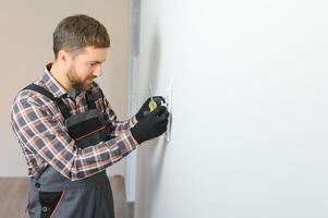 Electrician with screwdriver repairing power socket in room photo