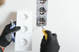 Confident professional electrician in uniform using screwdriver while replacing a socket in apartment after renovation work. photo
