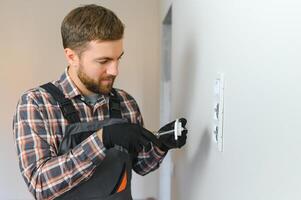 Electrician with screwdriver repairing power socket in room photo