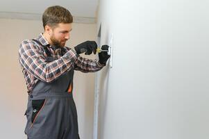 Electrician with screwdriver repairing power socket in room photo