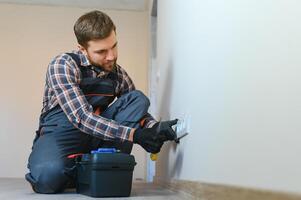 Confident professional electrician in uniform using screwdriver while replacing a socket in apartment after renovation work. photo