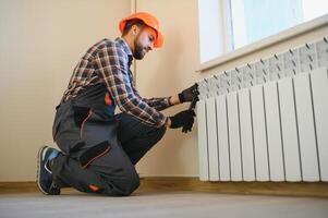 young man plumber checking radiator while installing heating system in apartment photo