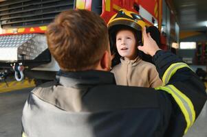 A fireman shows his work to his young son. A boy in a firefighter's helmet photo
