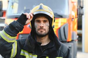 Portrait of a firefighter in a protective suit and a protective helmet standing by a fire engine after working on a fire. Close-up image photo