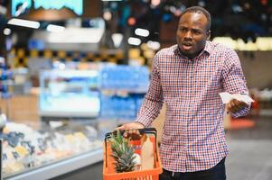 Surprised African-American man looks at receipt total in sales check holding paper bag photo