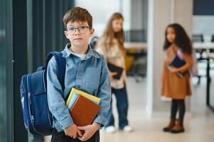Happy cute clever boy in glasses with school bag and book in his hand photo