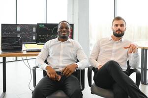 Two successful trader sitting in office, checking cryptocurrency information data on finance market graph, pointing on monitor photo