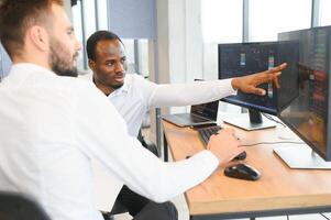 Two successful trader sitting in office, checking cryptocurrency information data on finance market graph, pointing on monitor photo