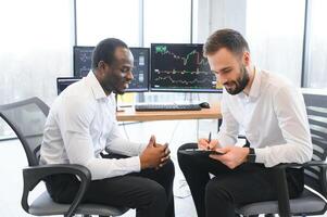 Two successful trader sitting in office, checking cryptocurrency information data on finance market graph, pointing on monitor photo