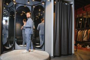 Modern young handsome businessman dressed in classical suit adjusting a tie in front of the mirror while standing in the suit shop photo