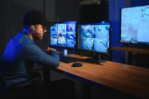 Rear view of security system operator looking at CCTV footage at desk in office photo