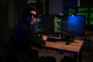hacker sitting at desk in dark atmosphere. A computer programmer or hacker. Anonymous computer hacker. photo
