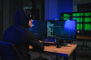 hacker sitting at desk in dark atmosphere. A computer programmer or hacker. Anonymous computer hacker. photo
