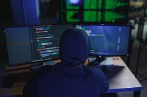 hacker sitting at desk in dark atmosphere. A computer programmer or hacker. Anonymous computer hacker. photo